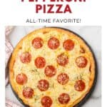 A round pepperoni pizza with melted cheese on a pan, next to a red and white towel.