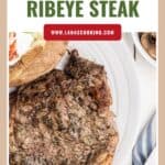 Grilled ribeye steak on a white plate with a baked potato and napkin beside it.