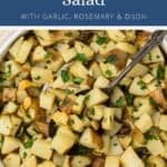 Roasted potato salad with garlic, rosemary, and Dijon in a serving bowl with a spoon.