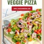 Sheet pan with roasted veggie pizza topped with spinach, tomatoes, onions, and peppers beside a pizza cutter.
