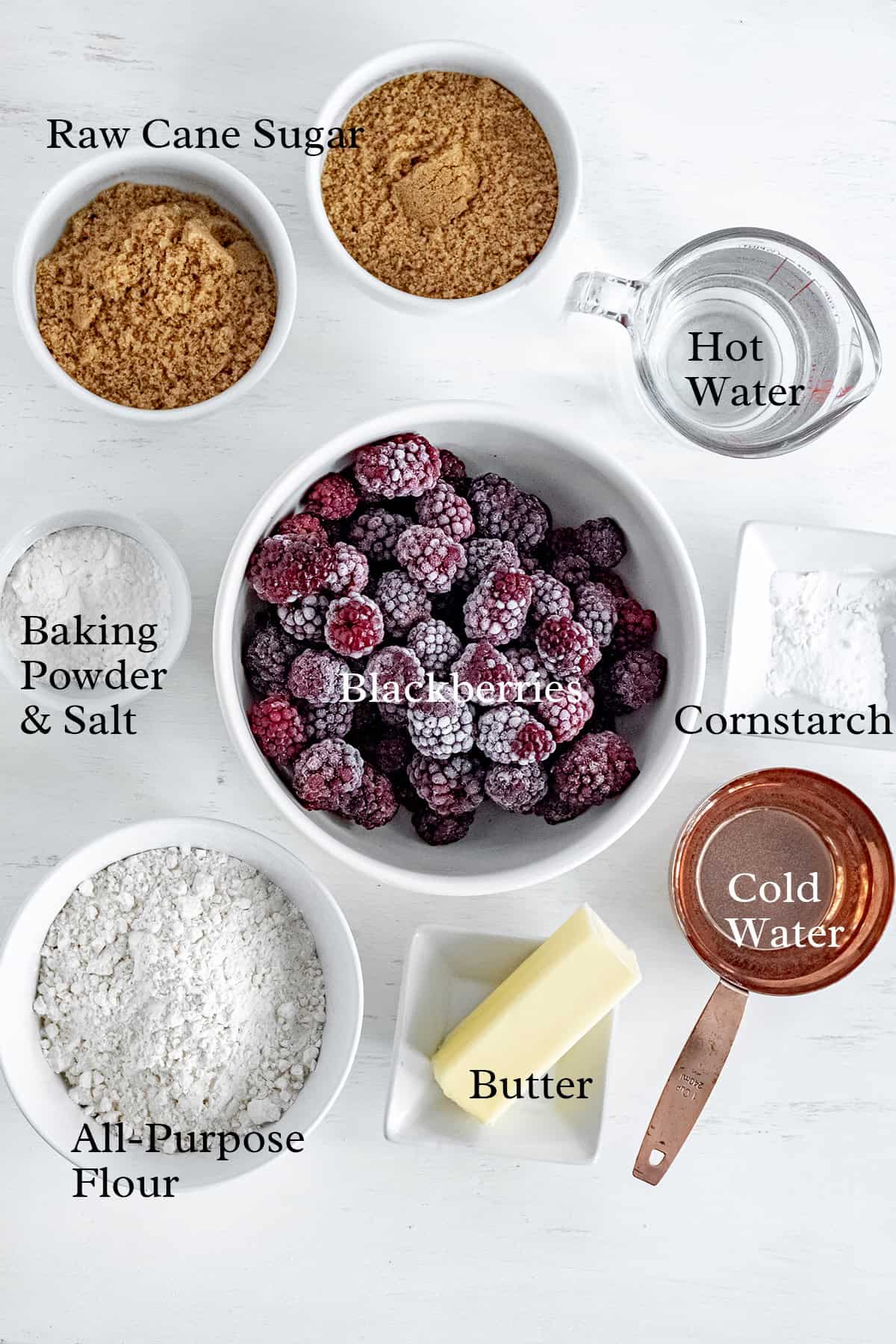 Overhead view of baking ingredients in bowls: blackberries, sugar, flour, cornstarch, butter, water, and seasonings.