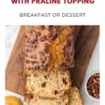 Apple bread with praline topping on a wooden board, two slices cut, apple and pecans beside it.