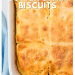 Golden brown butter swim biscuits in a white baking dish, shown close up with some biscuits cut into squares.