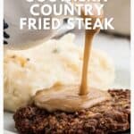 Gravy being poured over country fried steak with mashed potatoes in the background on a white plate.