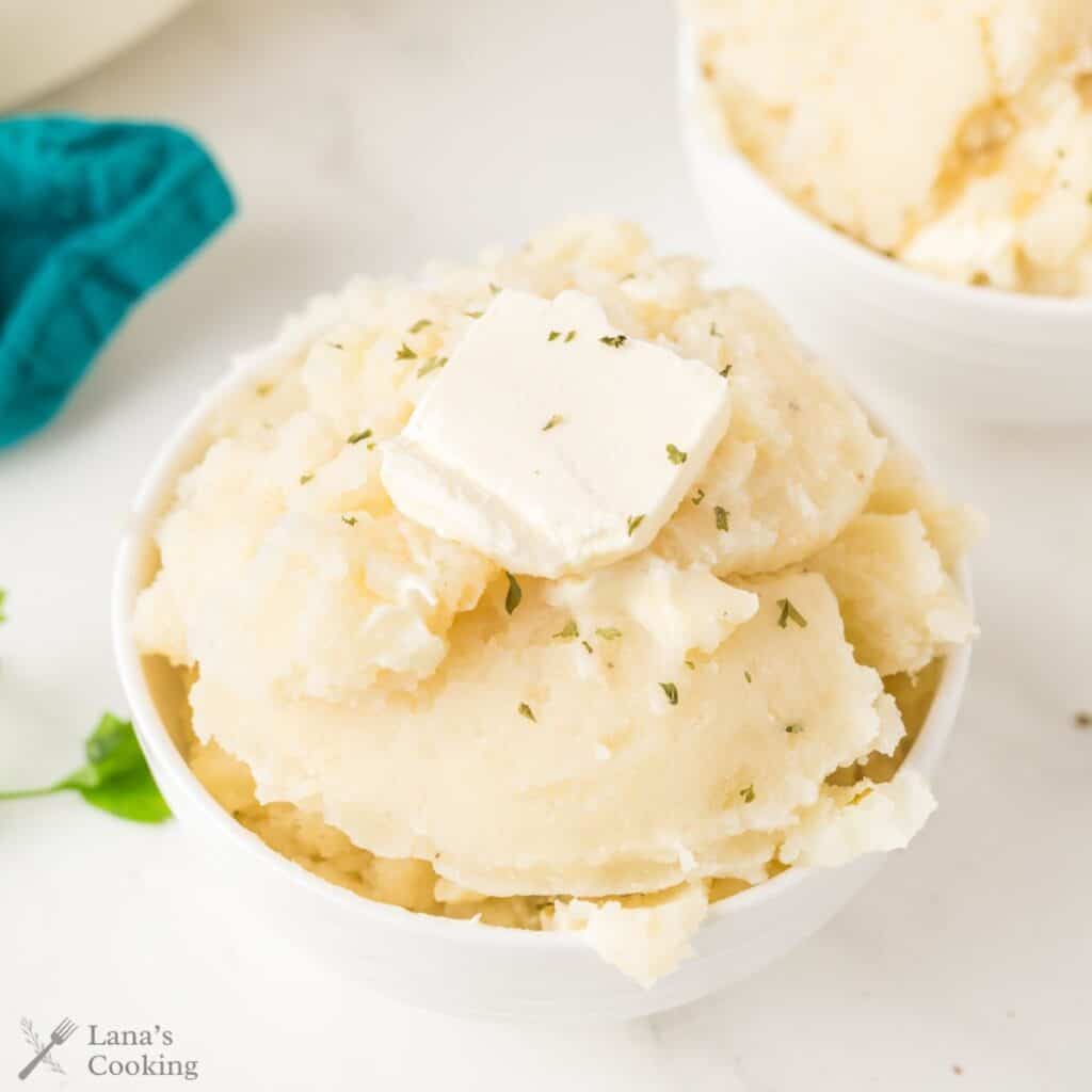 A bowl of mashed potatoes topped with a pat of butter and a sprinkle of herbs.