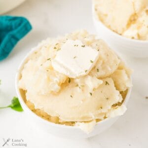 A bowl of mashed potatoes topped with a pat of butter and a sprinkle of herbs.