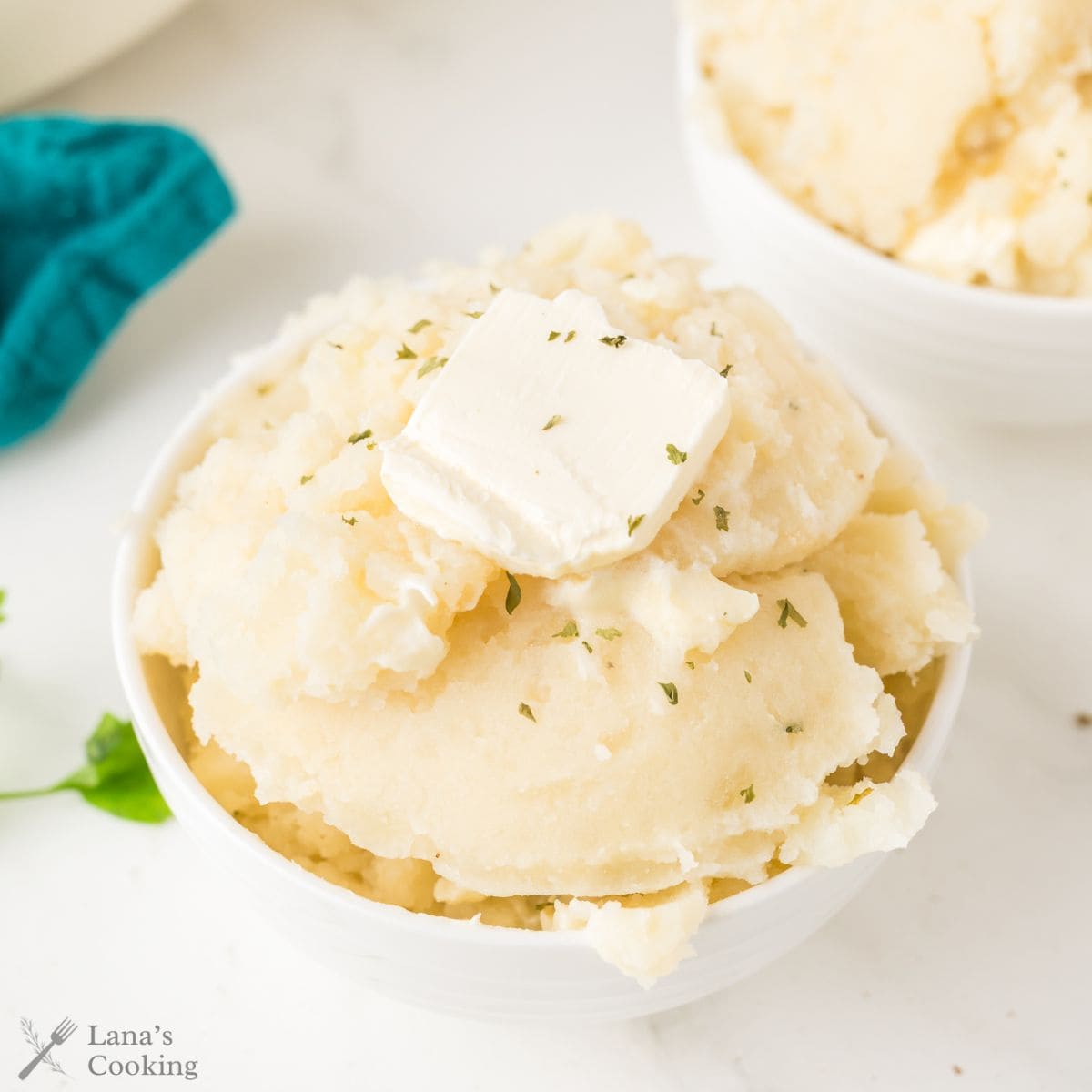 A bowl of mashed potatoes topped with a pat of butter and a sprinkle of herbs.