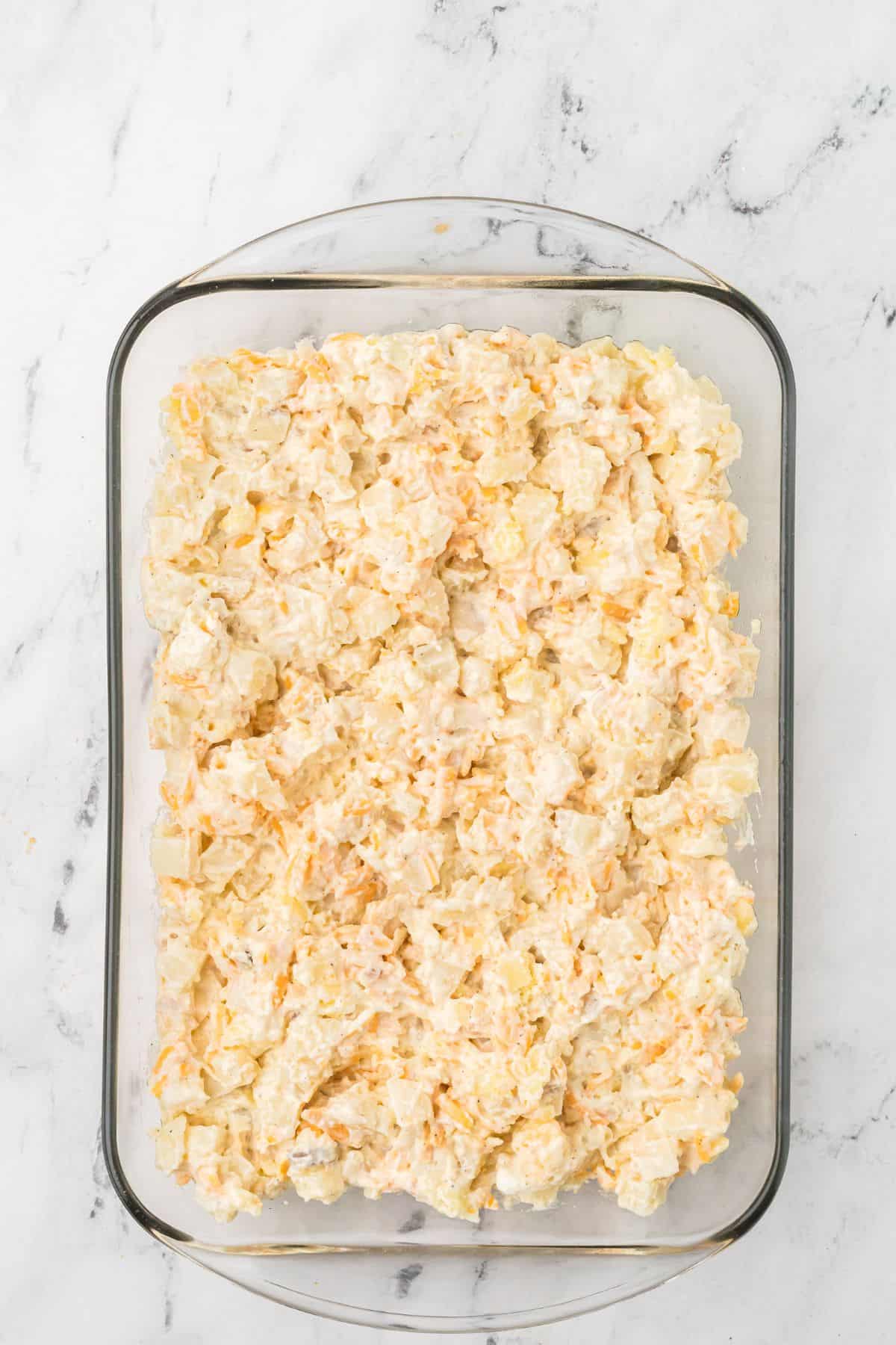 A glass baking dish filled with a creamy potato mixture on a white marble surface.