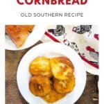 Plate of golden brown hot water cornbread on a wooden table, with a slice of ham and a chicken-patterned napkin.