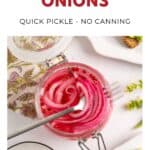 Open jar of pickled red onions with a fork, surrounded by spices and a floral napkin.