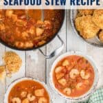 Overhead view of bowls and a pot of seafood stew with shrimp, and biscuits on a rustic table.