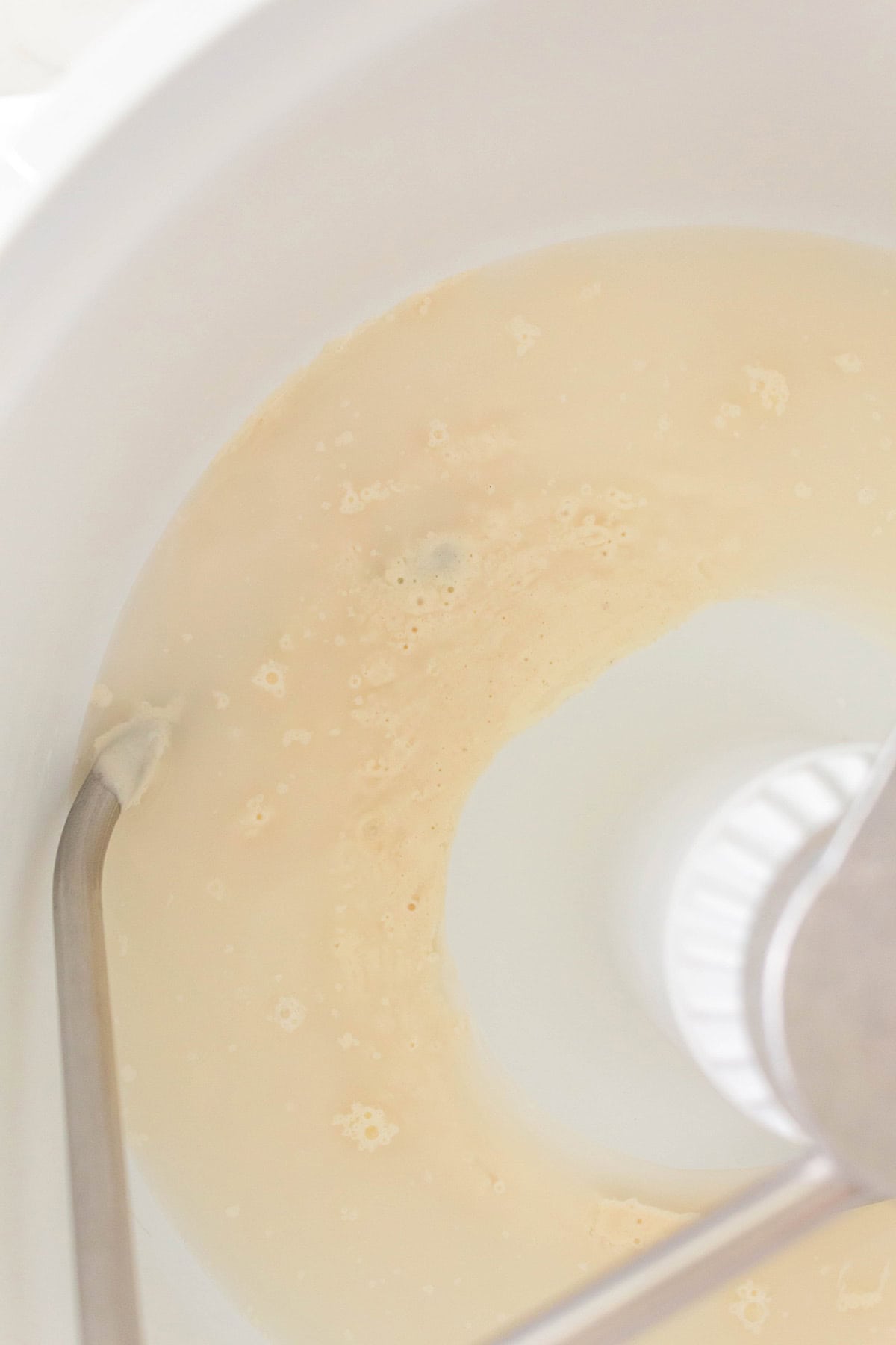 A close-up view of a stand mixer bowl containing sourdough starter and water with a mixing attachment visible on the left side.