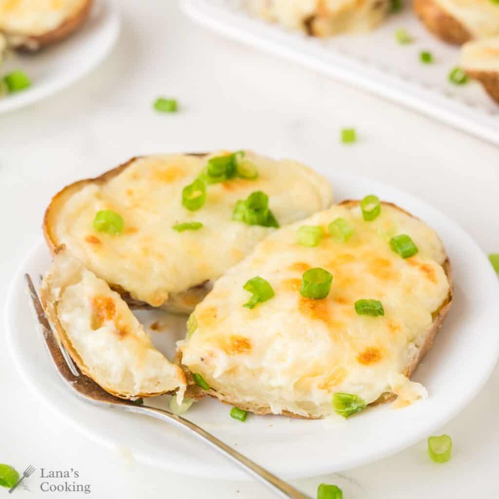 Two twice-baked potato halves topped with melted cheese and chopped green onions on a white plate.