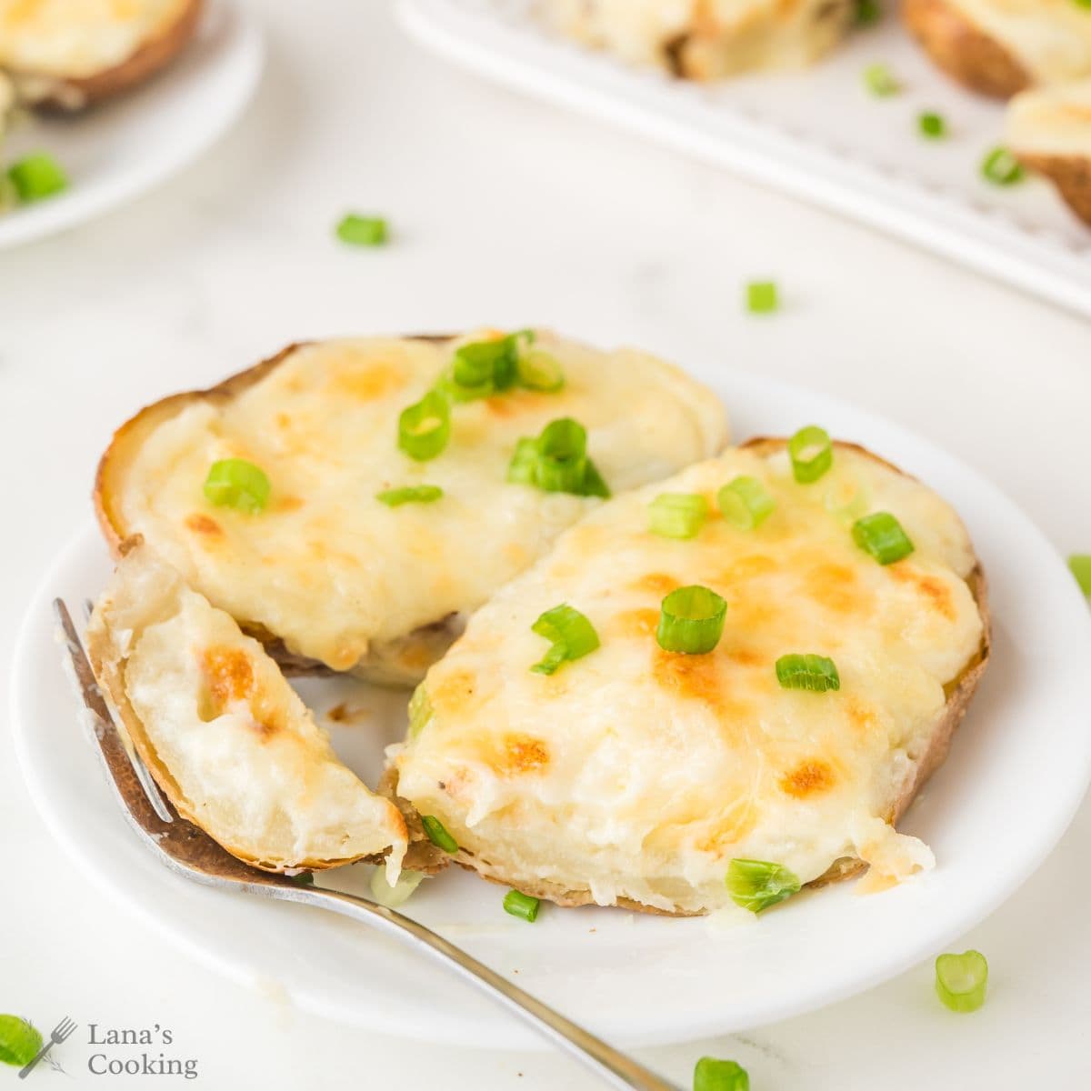 Two twice-baked potato halves topped with melted cheese and chopped green onions on a white plate.
