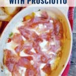 Oval baking dish with melted mozzarella and prosciutto, served on a red cloth with bread on the side.