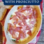 Oval dish of baked mozzarella with prosciutto, set on a red towel with slices of bread on the side.