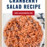 Shredded carrot and cranberry salad in a white bowl, topped with creamy dressing, on a marble surface.