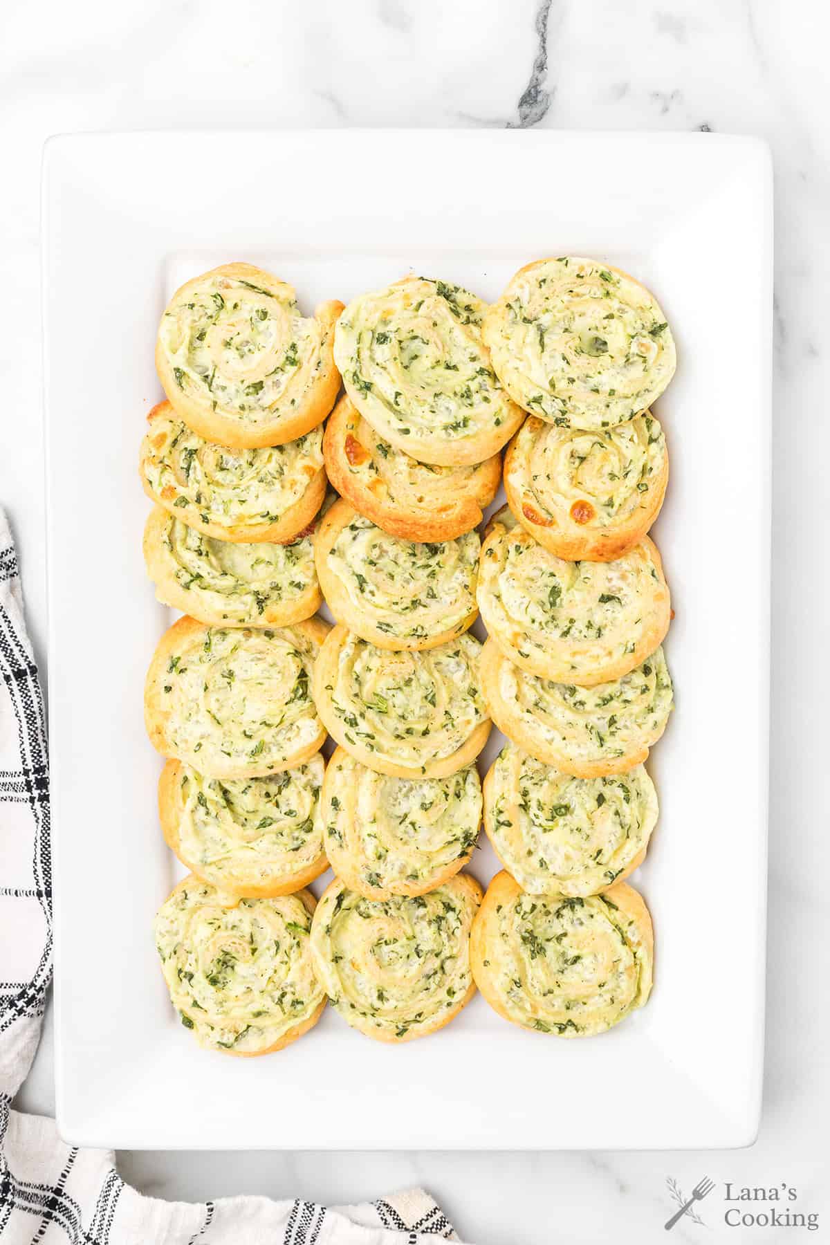 A rectangular white plate with neatly arranged spinach cheese pinwheels on a marble surface.