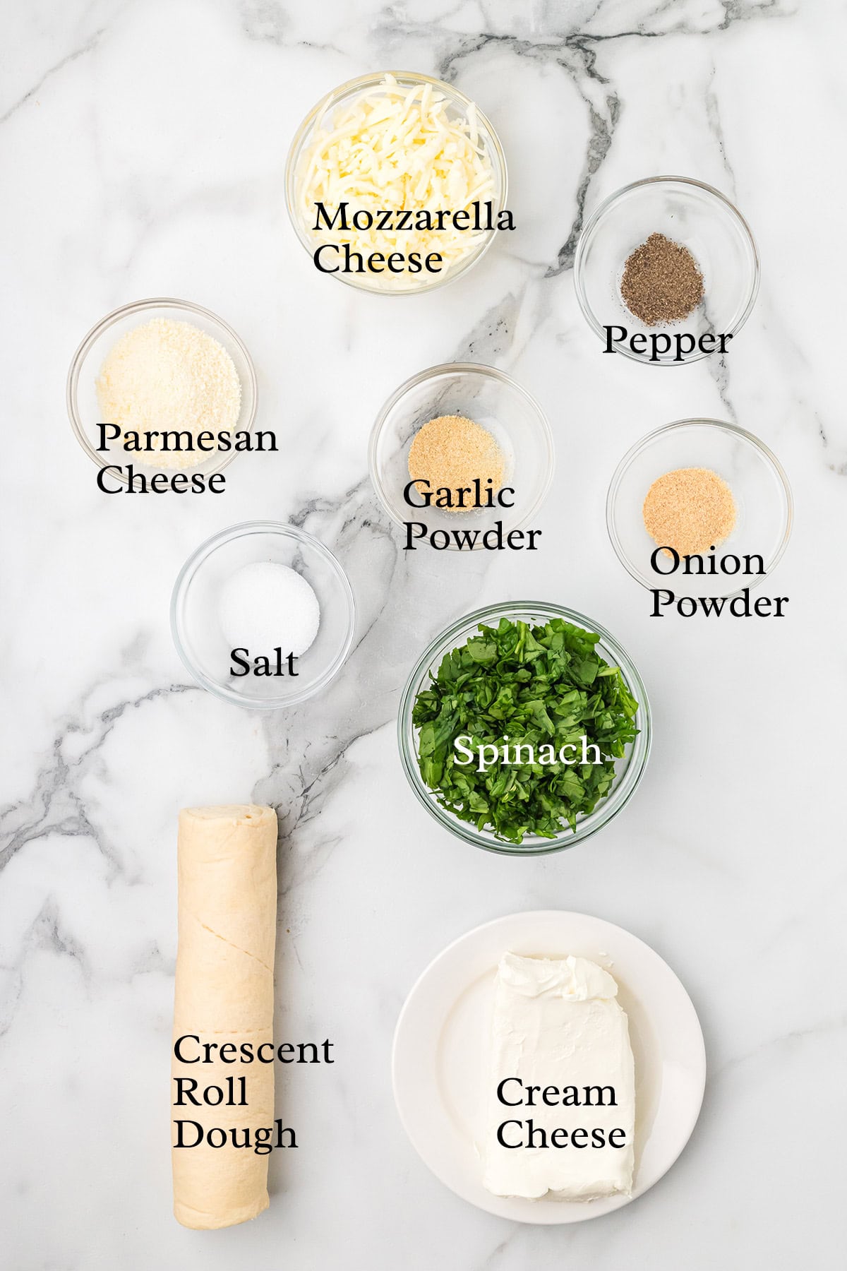 Ingredients on a marble surface: cheeses, spices, chopped spinach, crescent roll dough, and cream cheese.