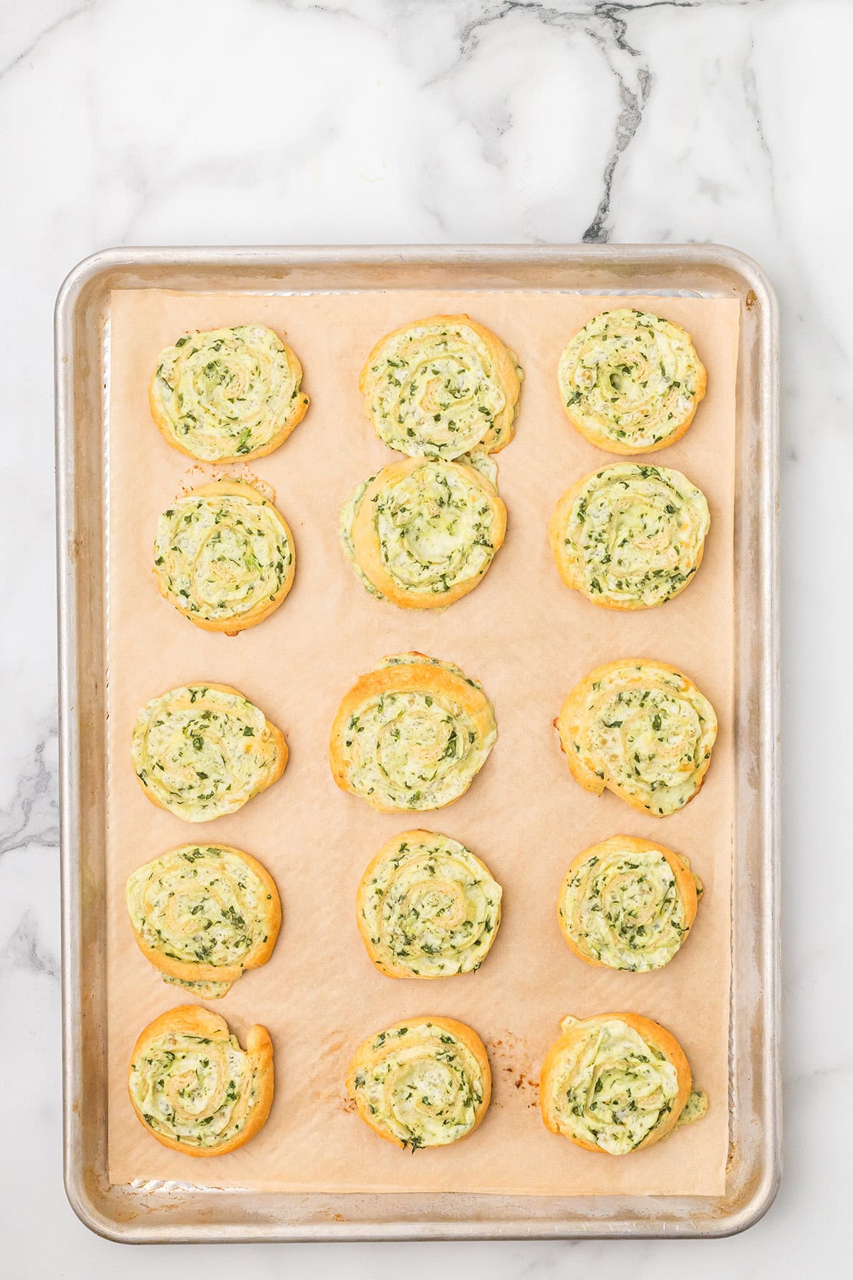 A baking sheet with 15 golden, spiral-shaped pinwheels on parchment paper.