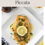 Classic chicken piccata topped with a lemon slice and capers on a white plate.