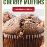 Chocolate cherry muffin with a cracked top, dusted with powdered sugar, shown close-up on a baking tray.