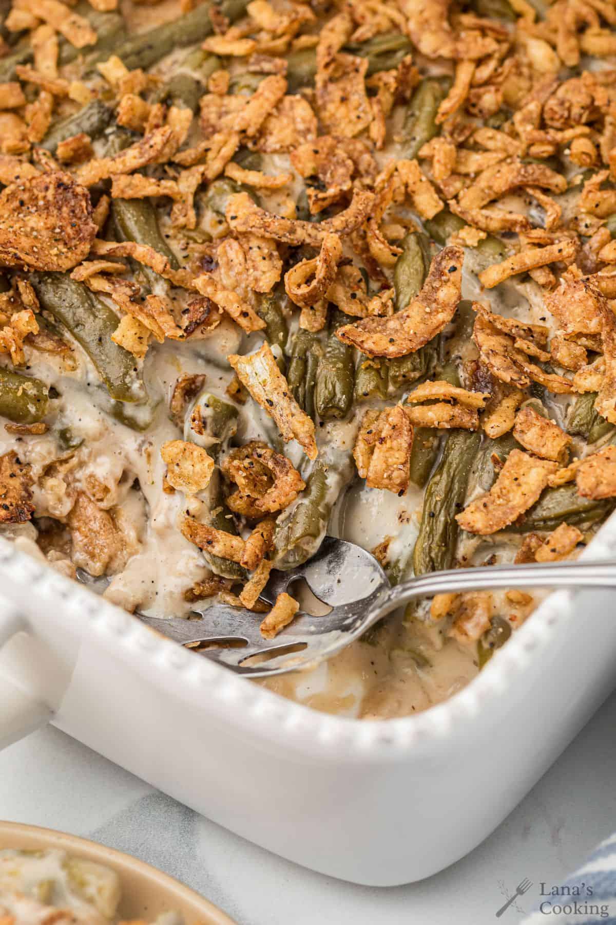 Green bean casserole topped with crispy fried onions in a white baking dish, with a serving spoon inside.