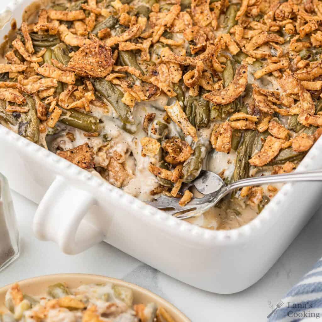 Green bean casserole in a white baking dish topped with crispy fried onions, with a fork inside.
