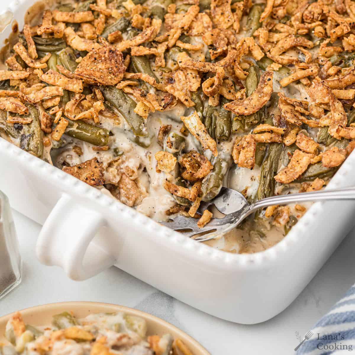 Green bean casserole in a white baking dish topped with crispy fried onions, with a fork inside.