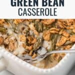 Baked green bean casserole with crispy onion topping in a white dish, with a serving spoon inside.