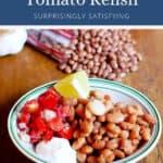A bowl of pinto beans with tomato relish, a lemon wedge, and sour cream.