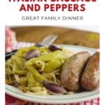 Plate of spaghetti topped with peppers, onions, and two sausages, on a checkered tablecloth.
