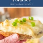 A hand holding a twice-baked potato topped with melted cheese and green onions.