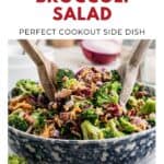 Large bowl of broccoli salad with bacon, cheese, and red onion, mixed with wooden salad servers.