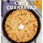Cast iron skillet with cheesy green chile cornbread, topped with a pat of butter.