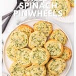 A plate of golden cheesy spinach pinwheels on a white surface, with forks and more pinwheels nearby.
