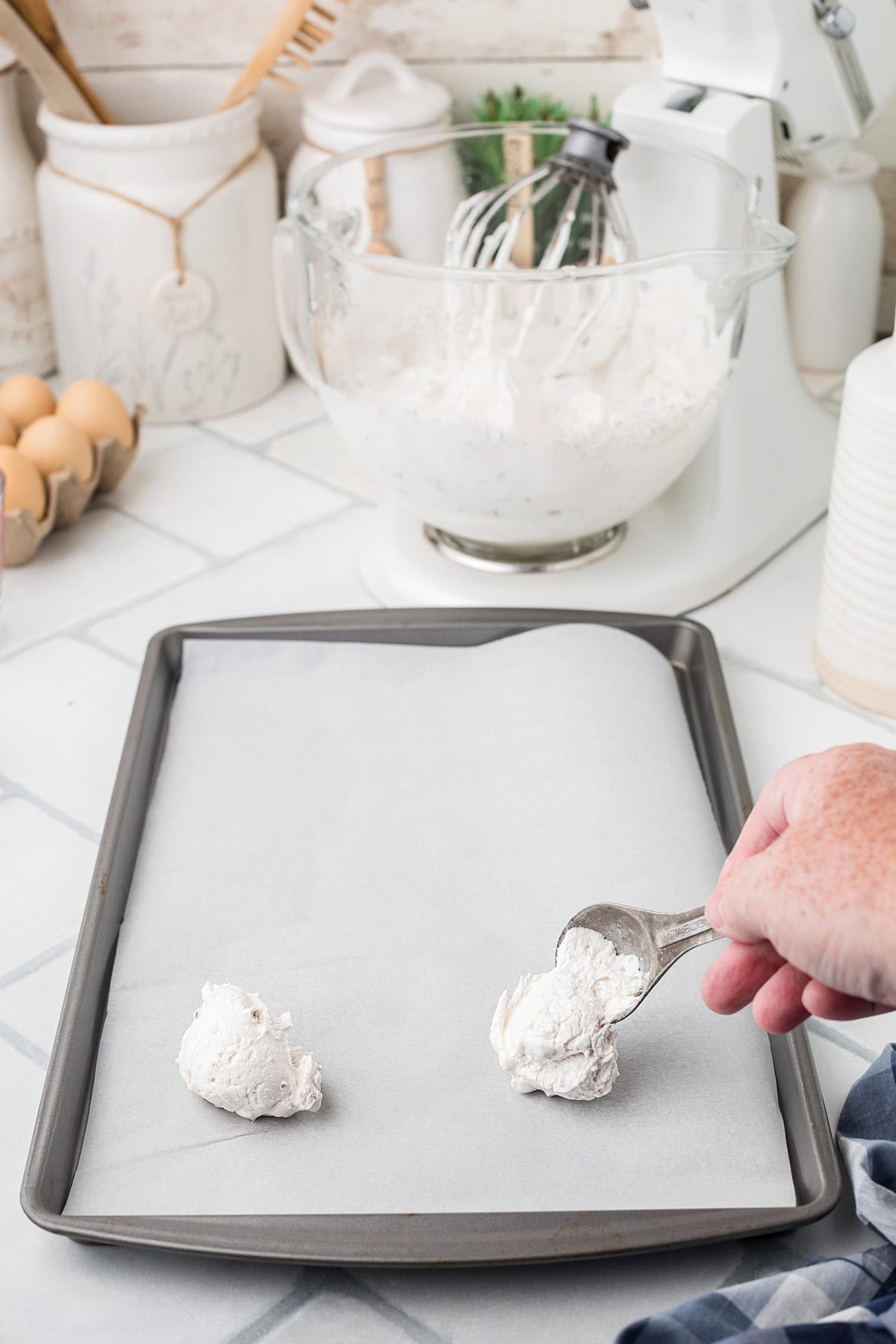 A hand scoops divinity candy onto a parchment-lined baking sheet in a kitchen.