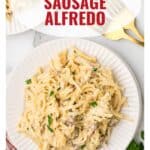 Plate of creamy Italian sausage Alfredo pasta on a white dish, with a fork and knife beside it.
