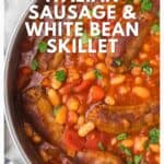 A skillet filled with Italian sausages, white beans, tomato sauce, and fresh herbs, seen from above.