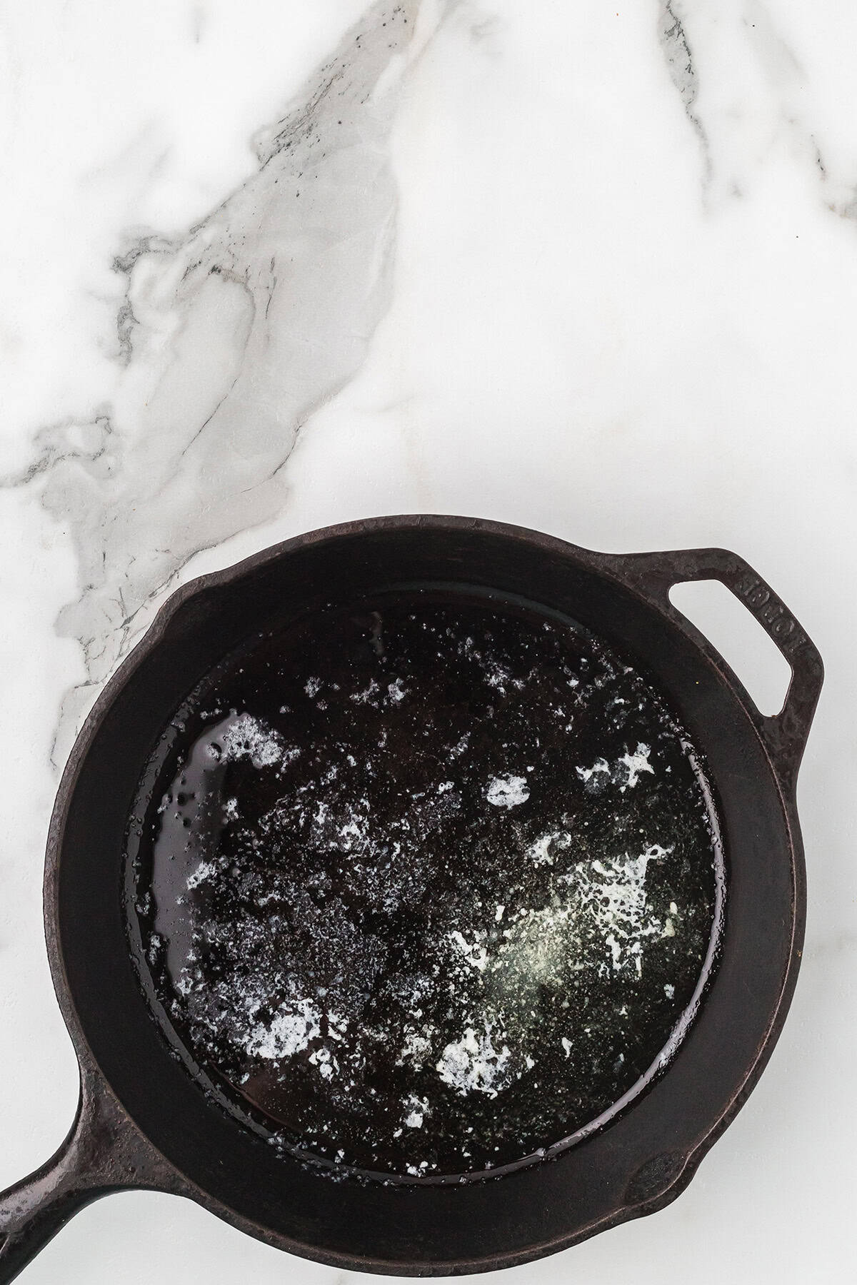A black cast iron skillet with melted butter sits on a white marble surface.