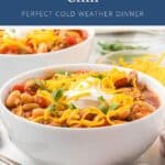 Bowl of white bean turkey chili topped with shredded cheddar cheese, sour cream, and herbs.