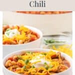 Two bowls of white bean turkey chili topped with shredded cheese, sour cream, and herbs.