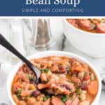 A white bowl of mixed bean and sausage soup with a black spoon.