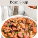 A bowl of hearty mixed bean and sausage soup topped with herbs.