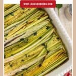 A baking dish filled with roasted leeks, seasoned with herbs and pepper.