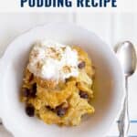 A bowl of bread pudding with raisins and whipped cream, next to a spoon, on a striped cloth.