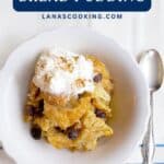 A bowl of bread pudding topped with whipped cream and raisins, with a spoon beside it on a striped cloth.