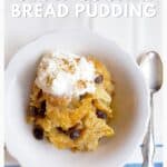 A bowl of bread pudding topped with whipped cream and cinnamon, shown with a spoon on the side.