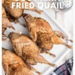 Six crispy fried quail arranged on a white platter with a salt shaker and checkered cloth nearby.