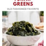 A bowl of cooked turnip greens sits on a wooden table with a fork and red checkered napkin nearby.